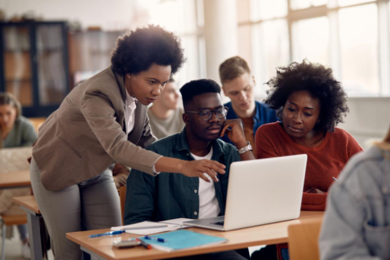 3 adults in the classroom looking at one laptop