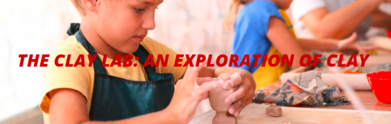 a child sitting at the table wearing an aprong and holding a block of clay